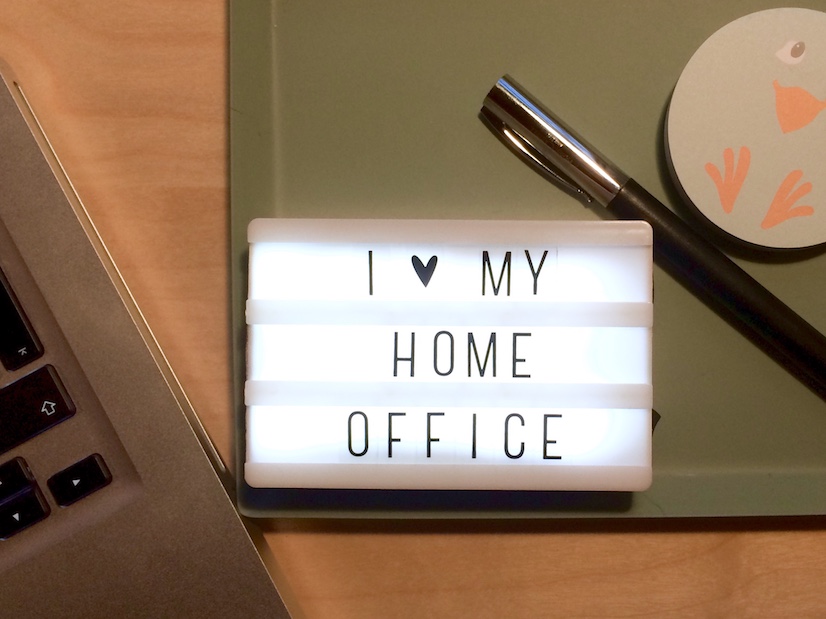 Eine kleine Lightbox mit dem Spruch "I love my Home-Office", Schreibutensilien und ein Mac auf dem Schreibtisch